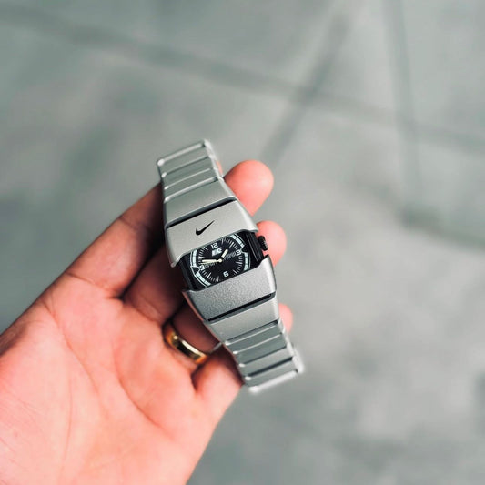 Hand holding a silver Nike watch with a blurred background